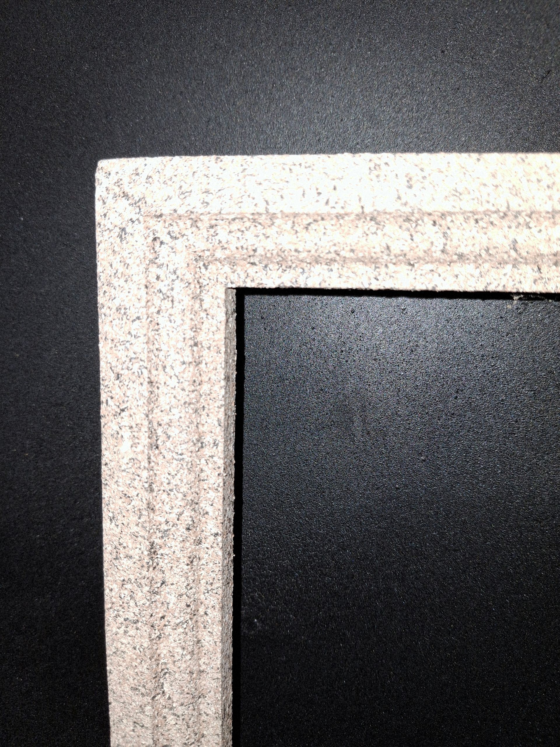 A close-up of a light-colored, textured picture frame border with a molded linear design against a black background.