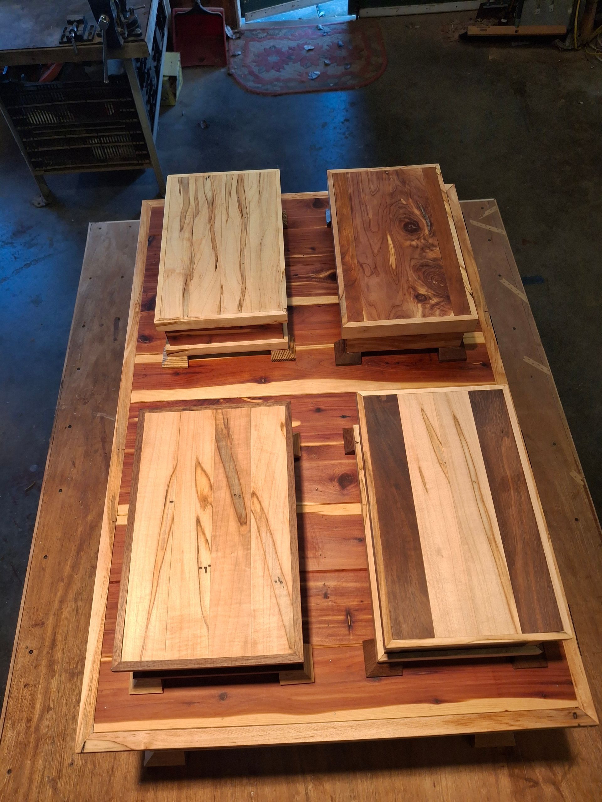 Four wooden boxes with varied light and dark wood grain lids, arranged on a rustic cedar wood table.