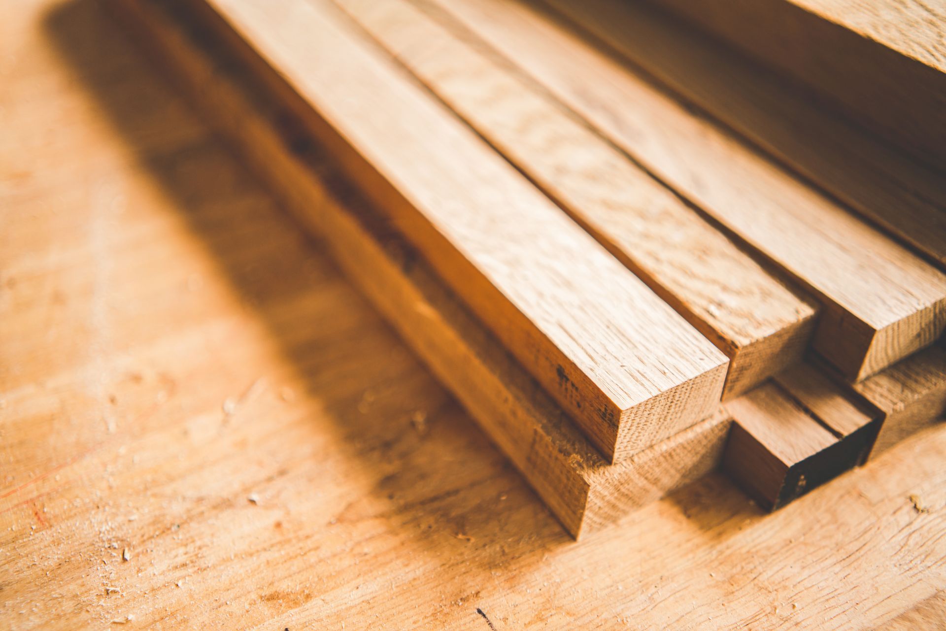 A close-up, high-angle shot of several light-colored wooden planks stacked diagonally on a textured wooden surface.
