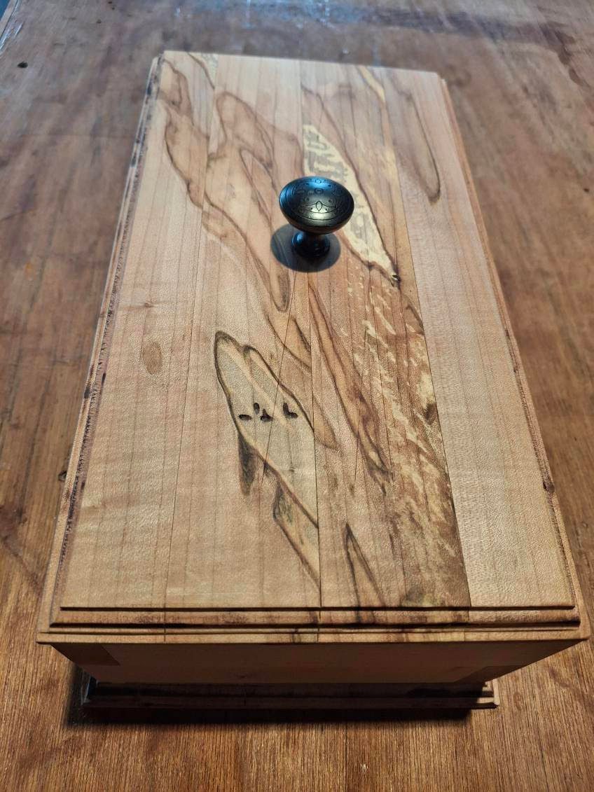 Wooden box with a carved lid and a dark knob on top, sitting on a wooden surface