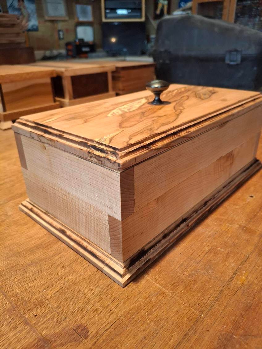 Small ornate wooden box with a carved lid and knob, sitting on a wooden table.