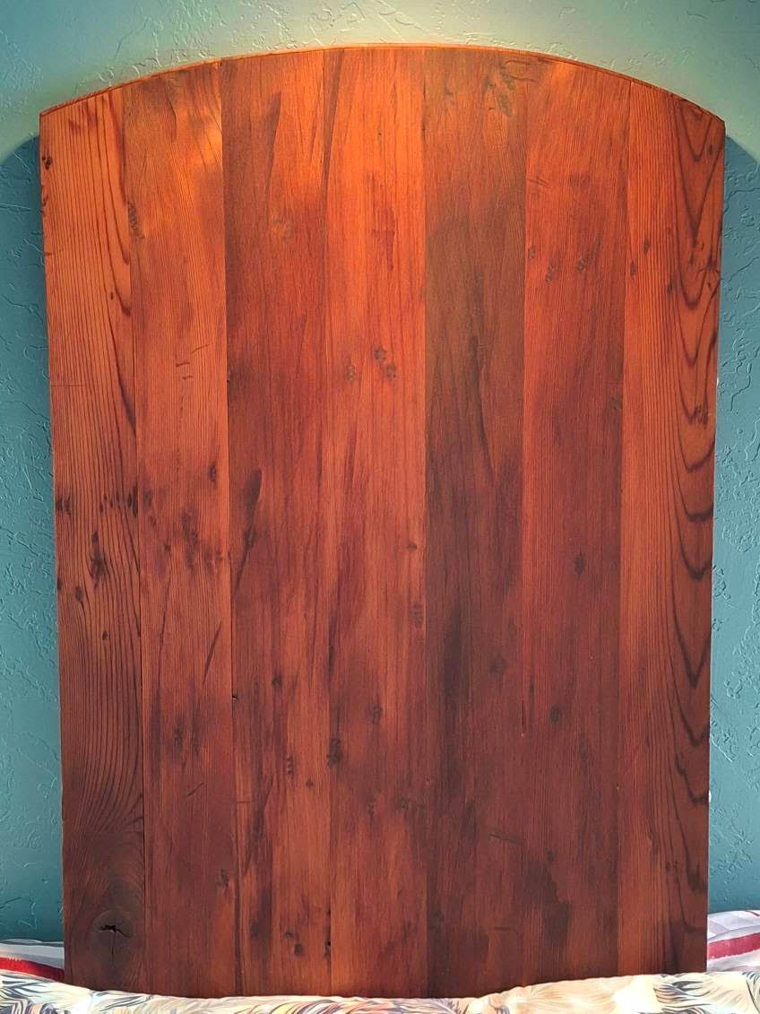 Curved wooden board with a reddish-brown finish against a teal wall