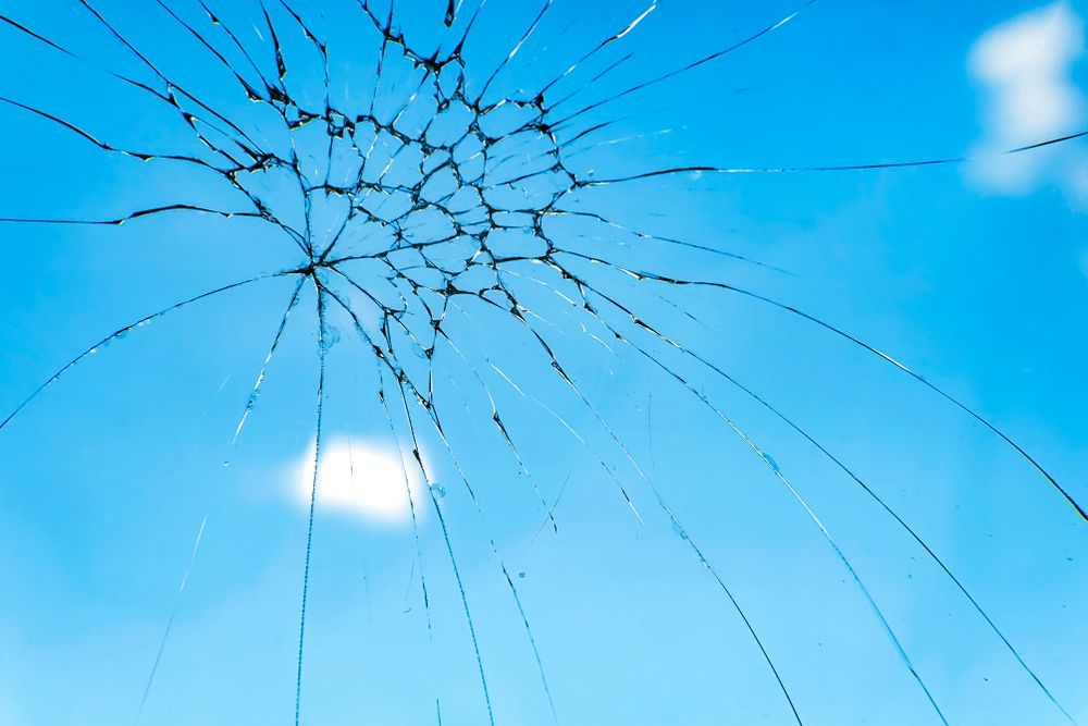 A Close Up of a Broken Glass Window With a Blue Sky in the Background — Crakka Windscreens in Harrington, NSW