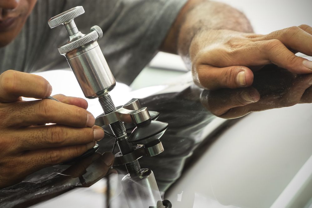A Man is Working on a Car Windshield With a Tool — Crakka Windscreens in Taree, NSW
