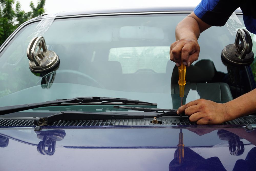 A Man is Fixing a Windshield on a Car With a Screwdriver — Crakka Windscreens in Diamond Beach, NSW