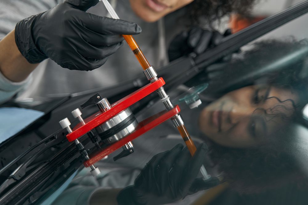 A Man is Repairing a Windshield on a Car With a Tool — Crakka Windscreens in Old Bar, NSW