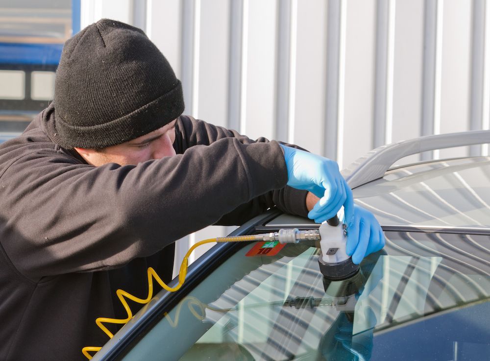 A Man is Repairing a Windshield on a Car — Crakka Windscreens in Taree, NSW