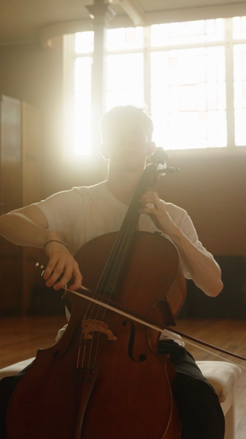 A man is playing a cello in a dark room.