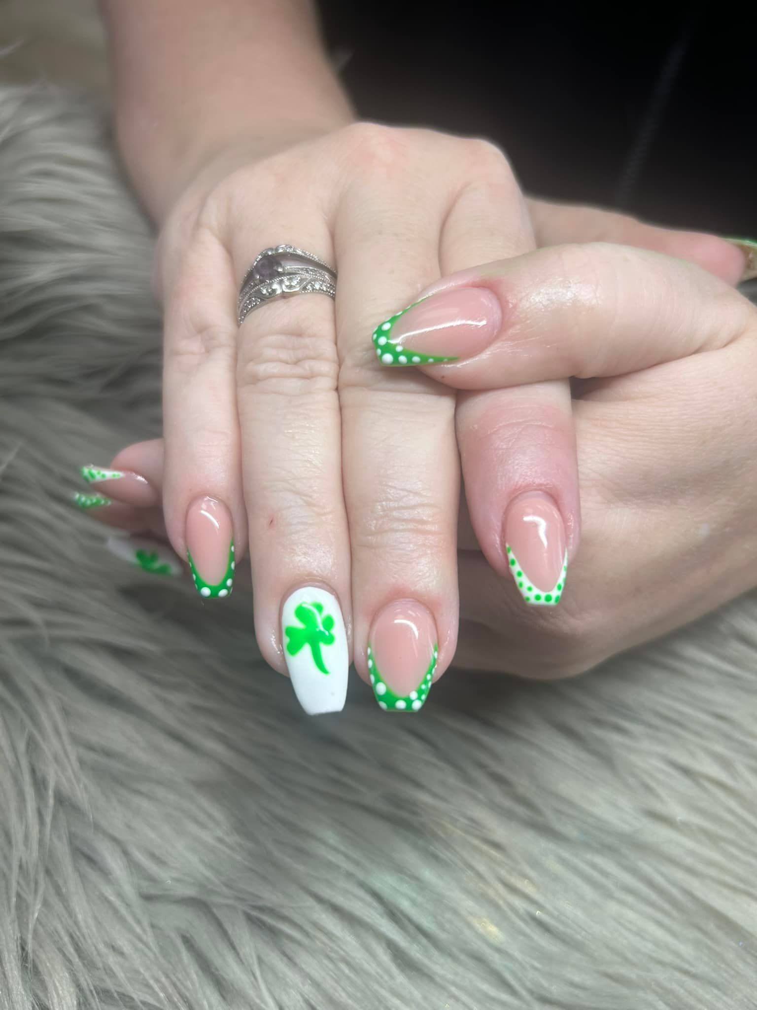 A woman 's nails are painted green and white with a clover design.