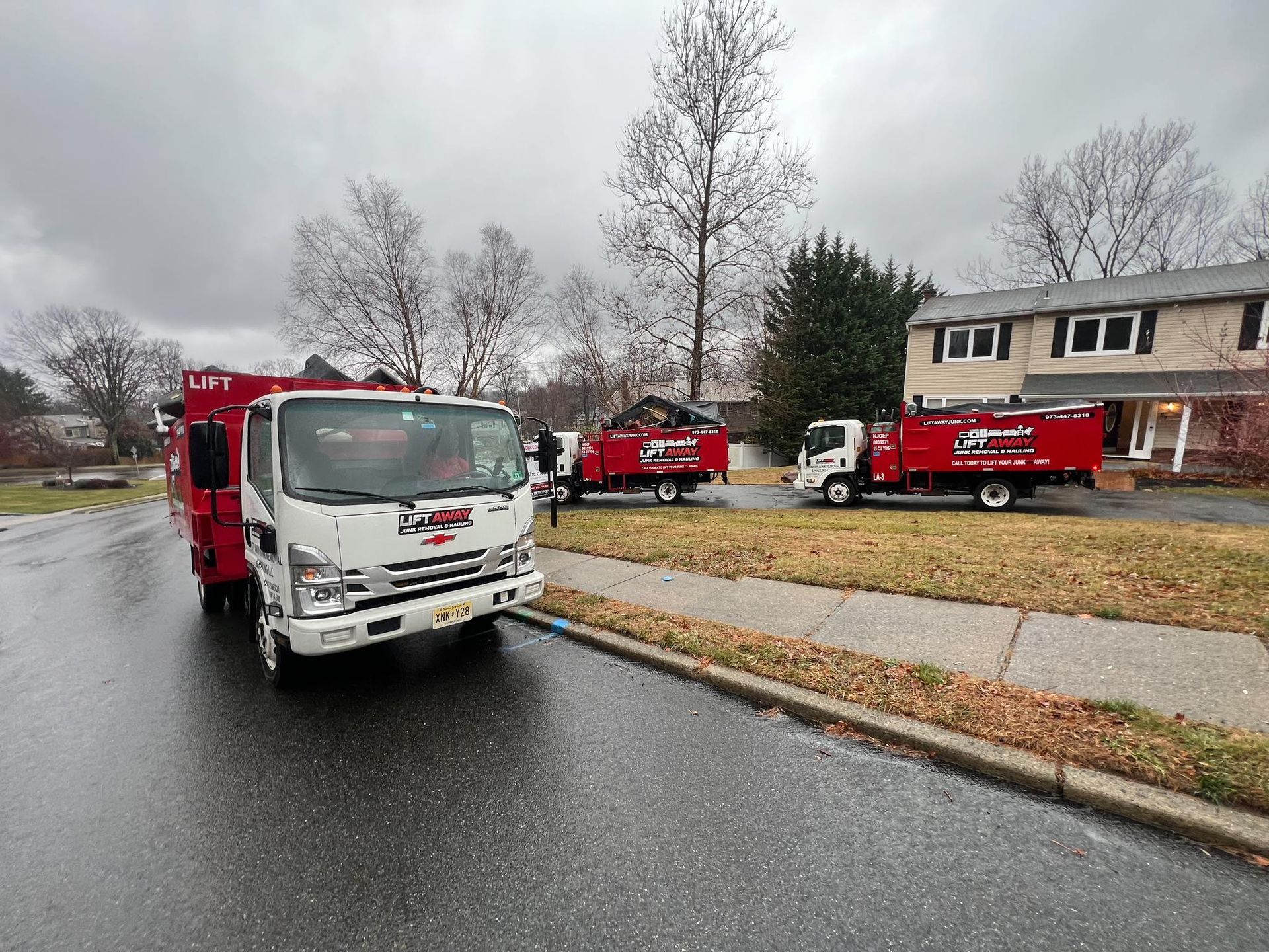 Three red and white tree service trucks parked near a house on a wet, overcast day.