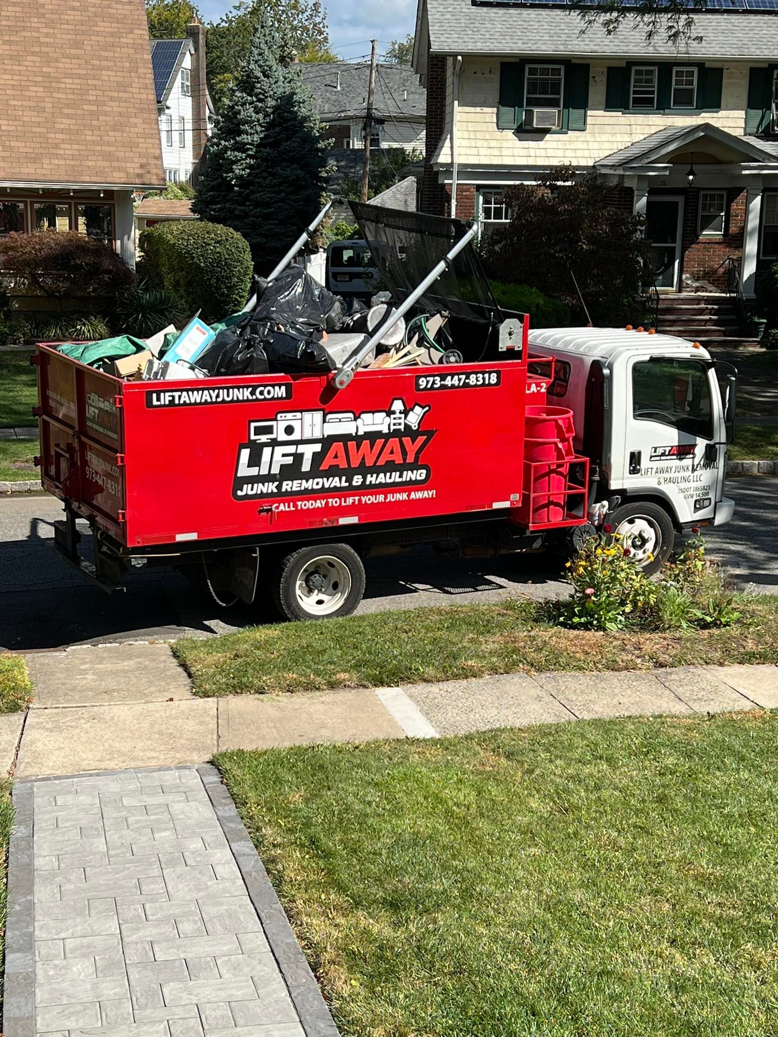 Red Lift Away junk removal truck parked on a residential street, loaded with debris.