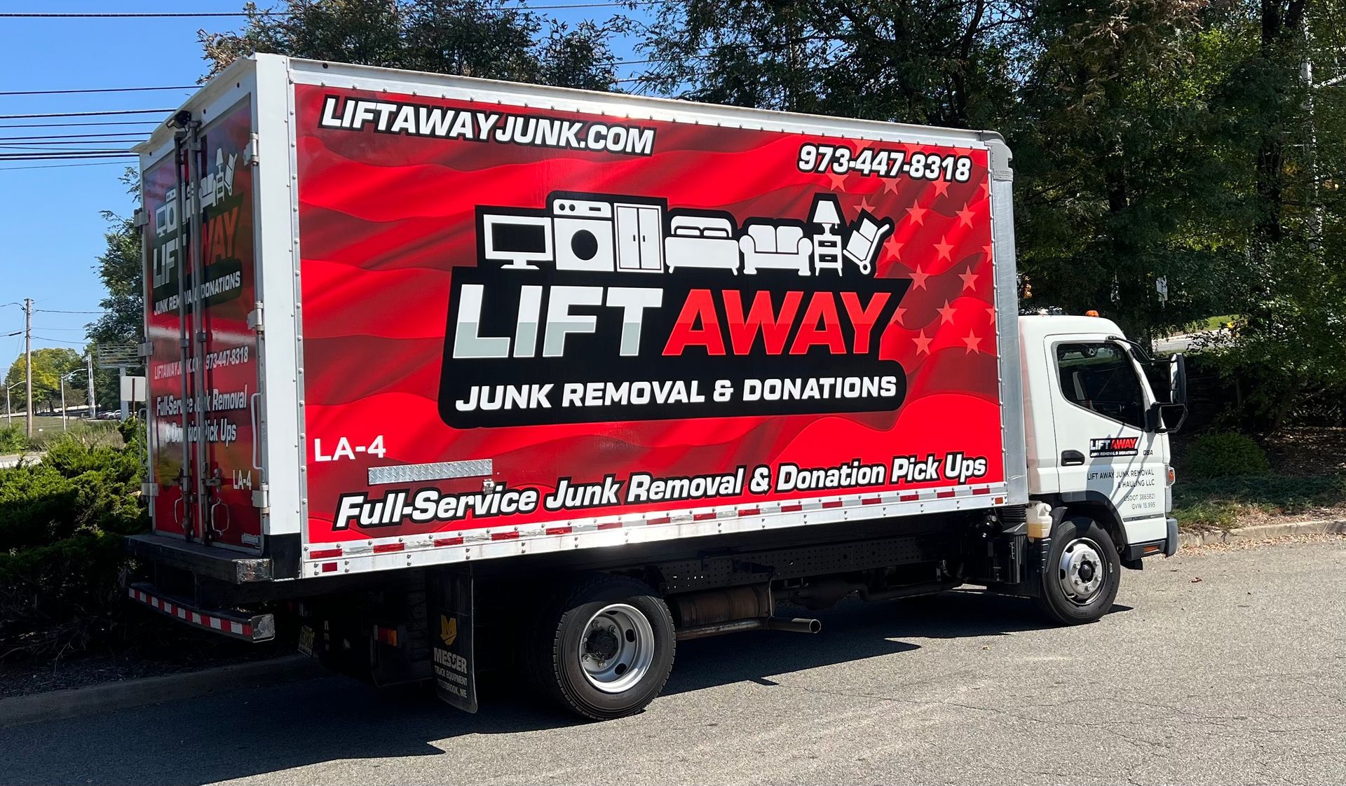 Two people in red shirts walk toward a white truck with a red aerial lift in front of a brick building.