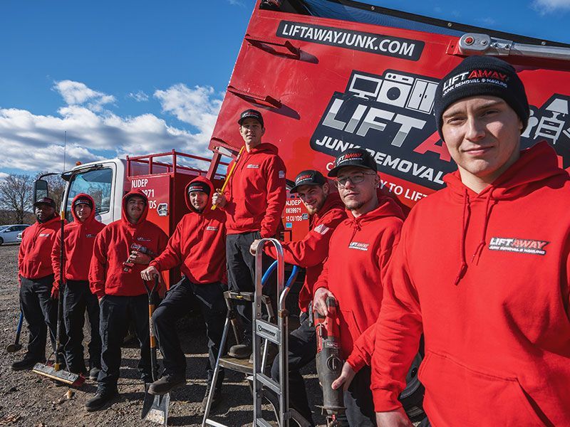 Group of people in red hoodies stand on a red truck, advertising junk removal services.