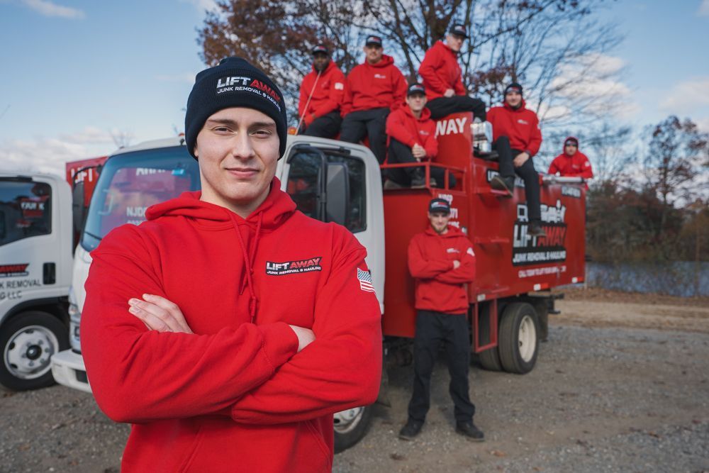 A man in a red hoodie and black beanie stands in front of a truck with a crew of people in red hoodies.