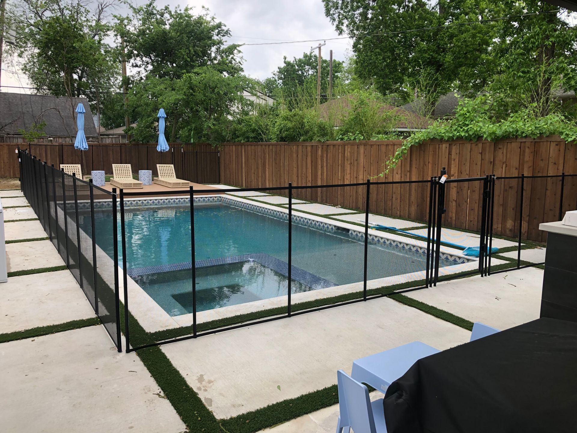 Fenced backyard with rectangular swimming pool, lounge chairs, and concrete patio with greenery around it