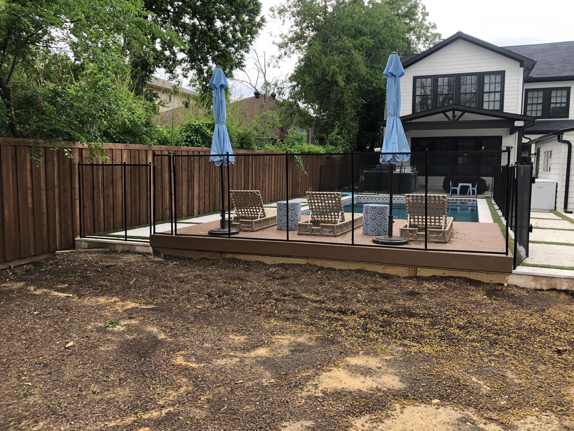 Backyard patio with wooden deck, black railings, blue umbrellas, and outdoor seating beside a house