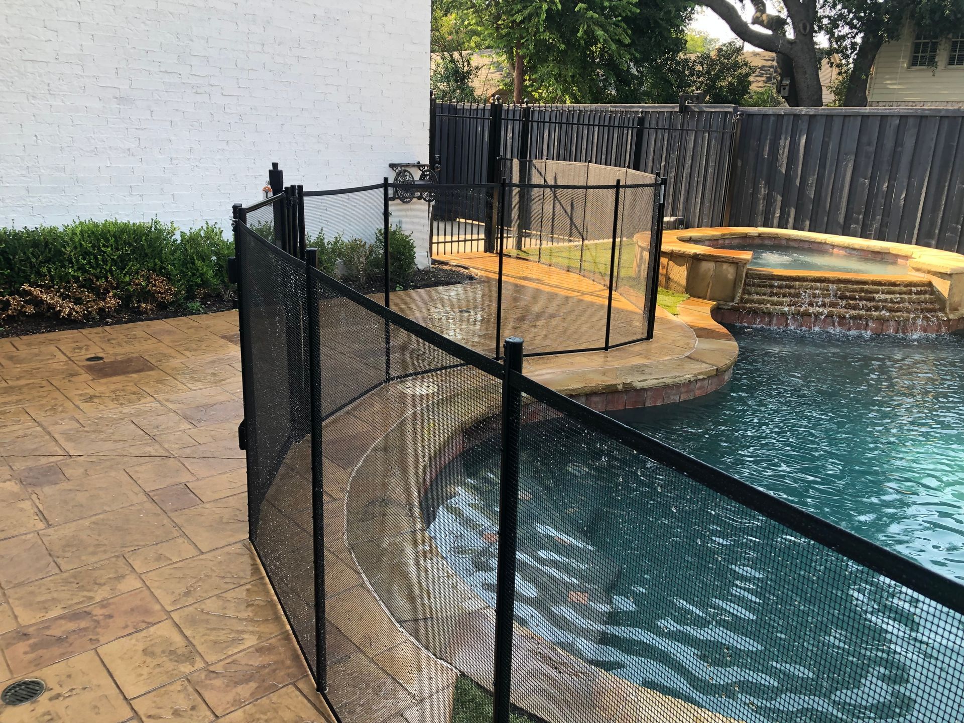 Poolside fenced walkway beside a blue swimming pool and stone patio