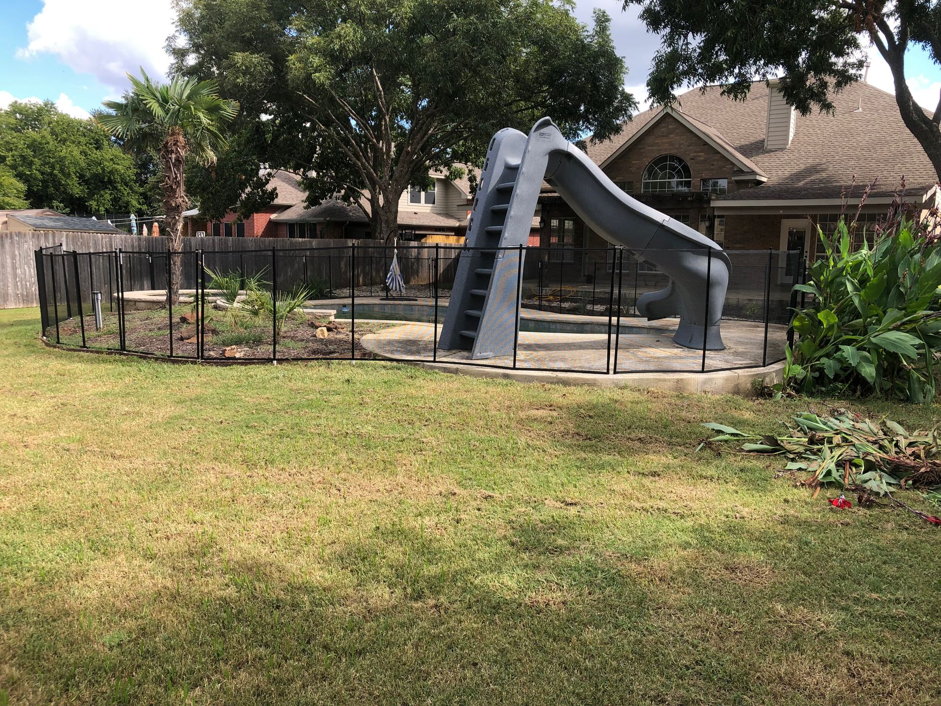 Backyard playground with a gray slide, fenced play area, and trees beside a house
