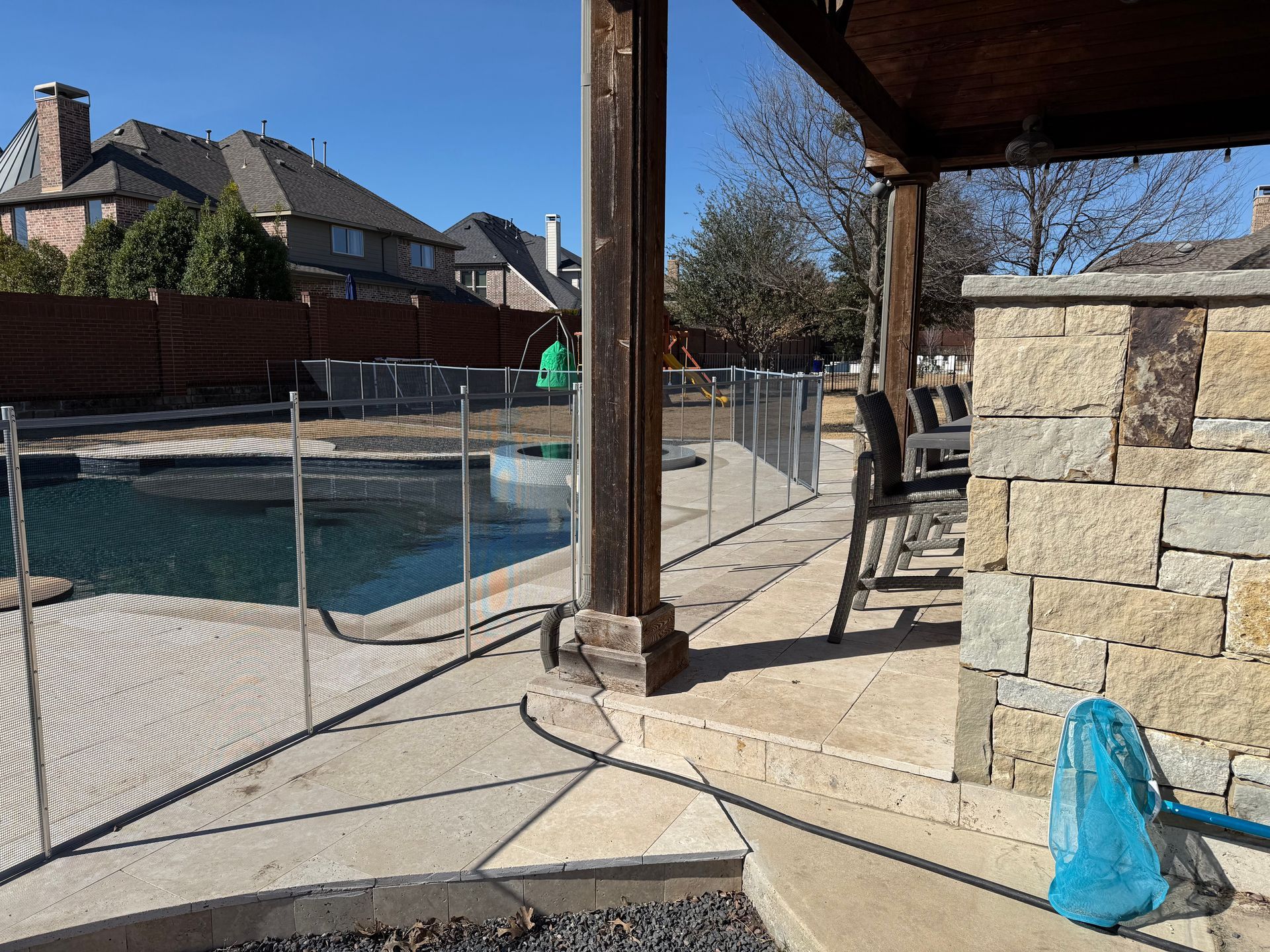 Backyard patio with pool fence, stone wall, and blue bag near a covered seating area