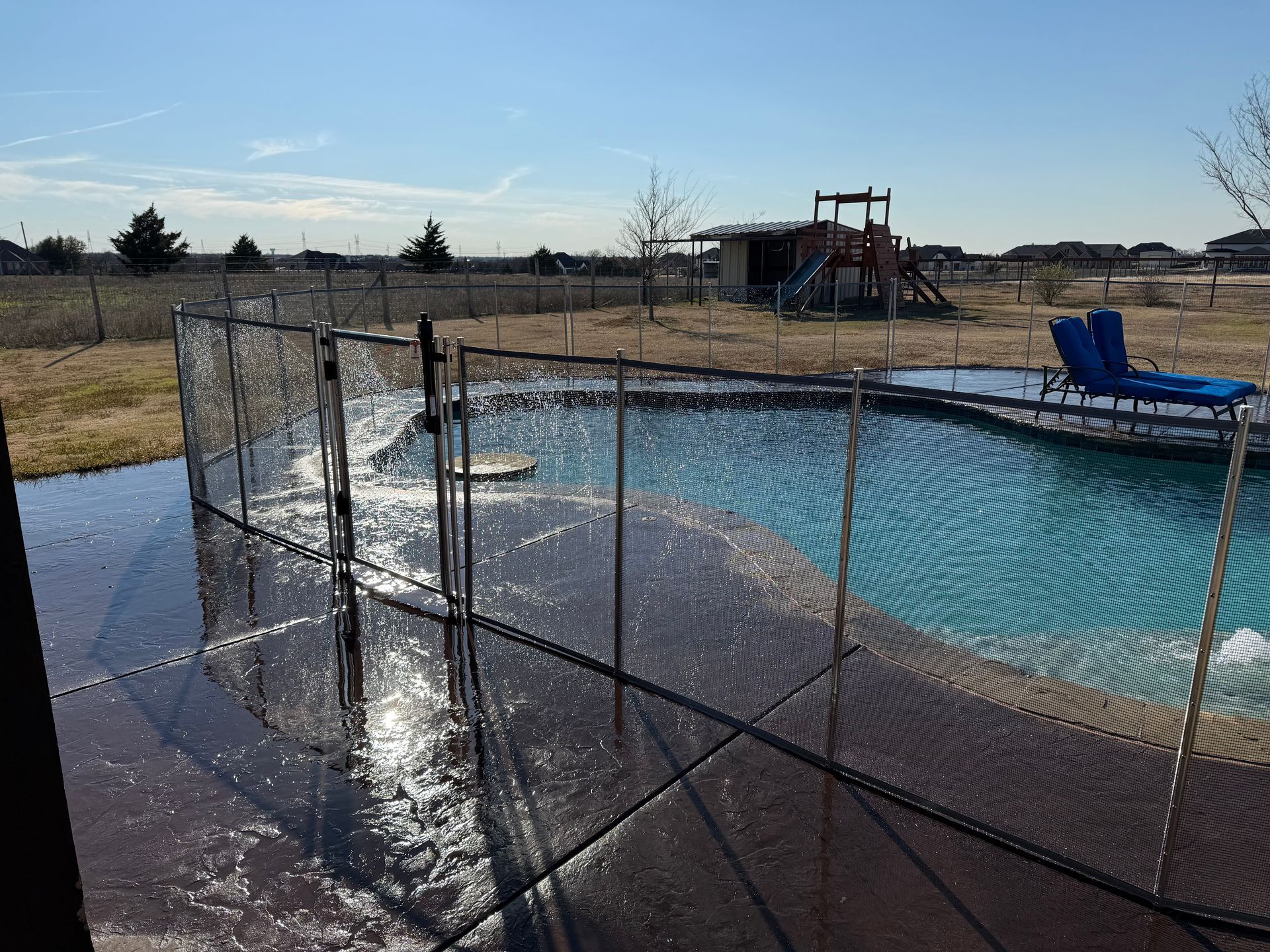 Backyard pool with chain-link fence and wet deck in bright sunlight