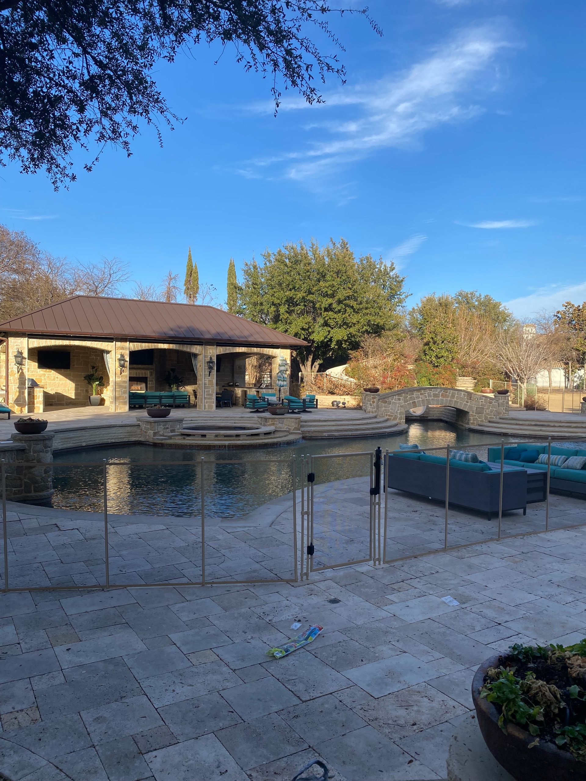 Backyard pool and spa with stone patio, beige house, and blue sky on a sunny day