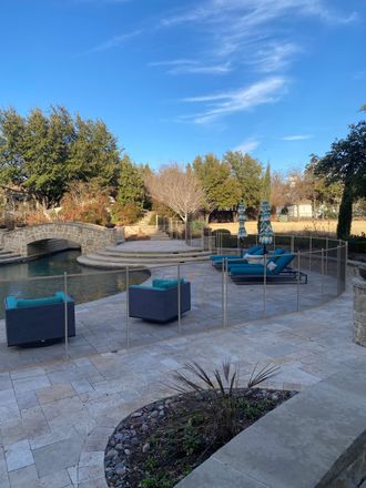 Outdoor patio with blue lounge chairs, potted plants, and a stone fire pit beside a pool under a clear sky
