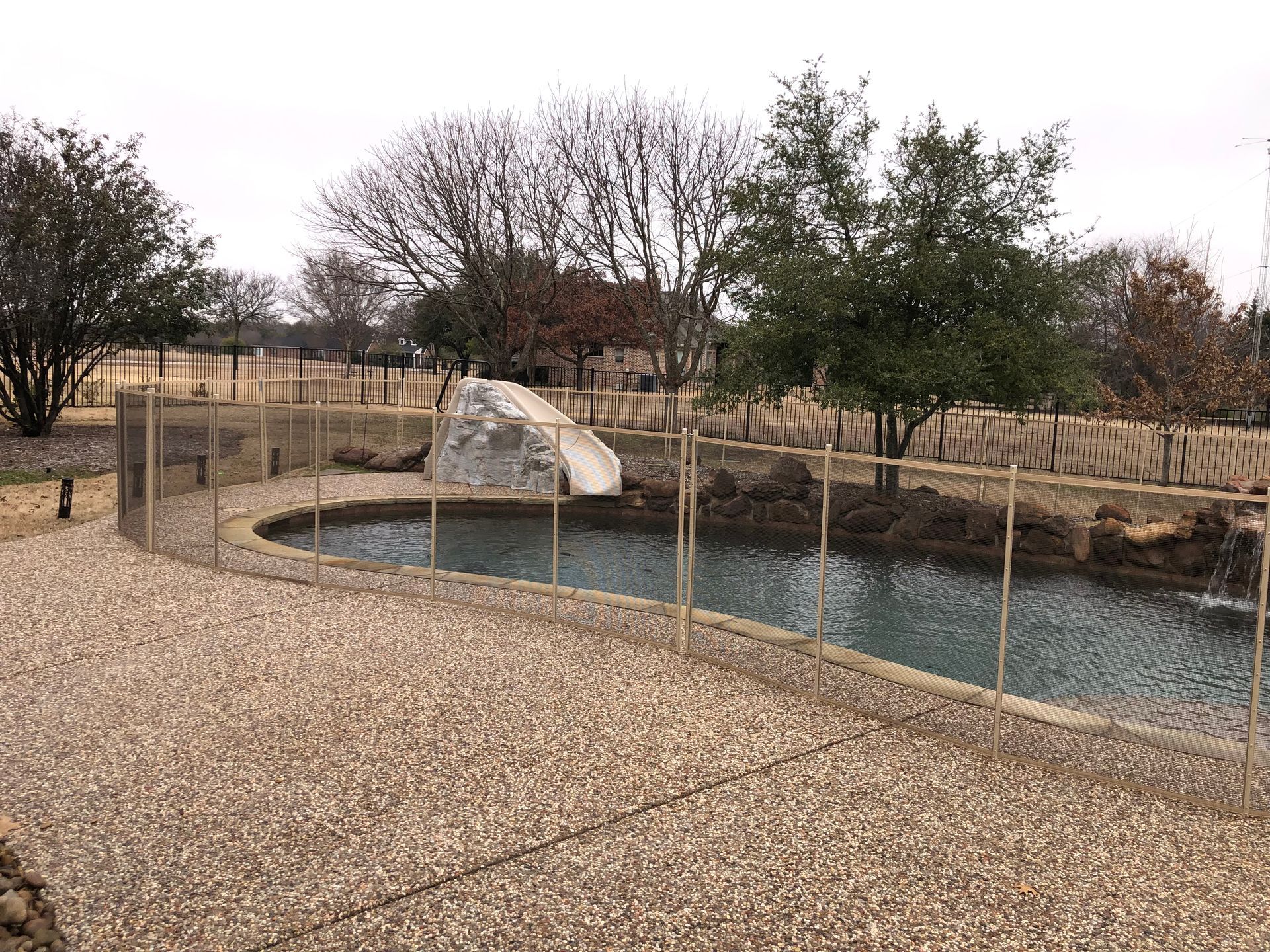 Gravel path beside a fenced pond with rocks and trees in a dry park landscape