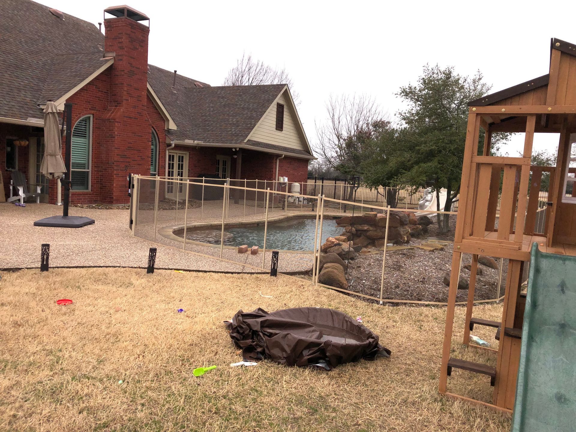 Backyard with a house, pool, stone patio, and a fire pit in the foreground