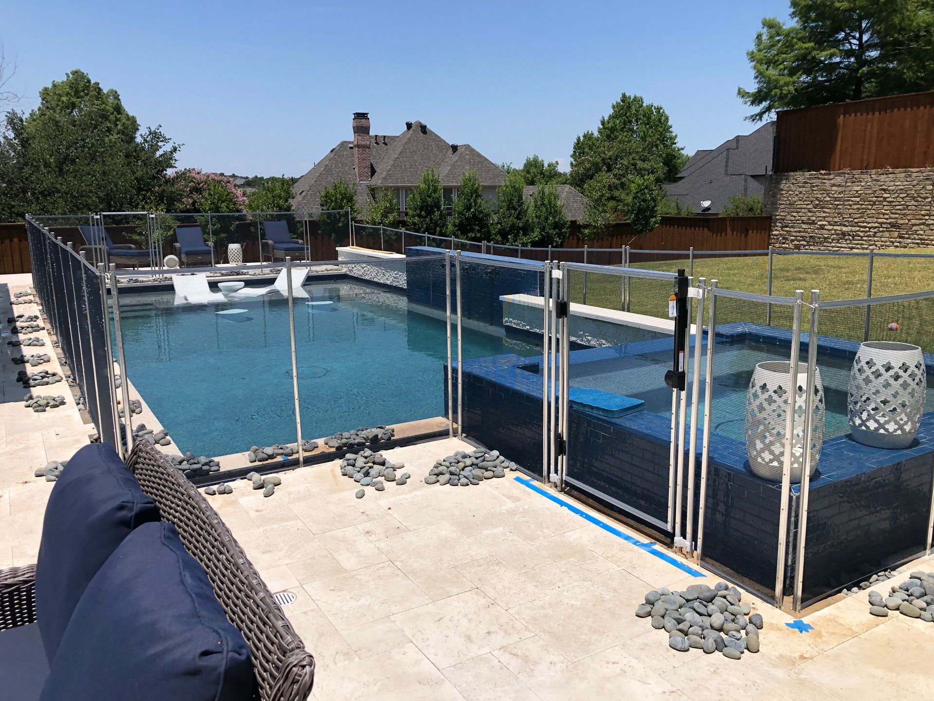 Backyard swimming pool surrounded by a glass safety fence and deck chairs on a sunny day
