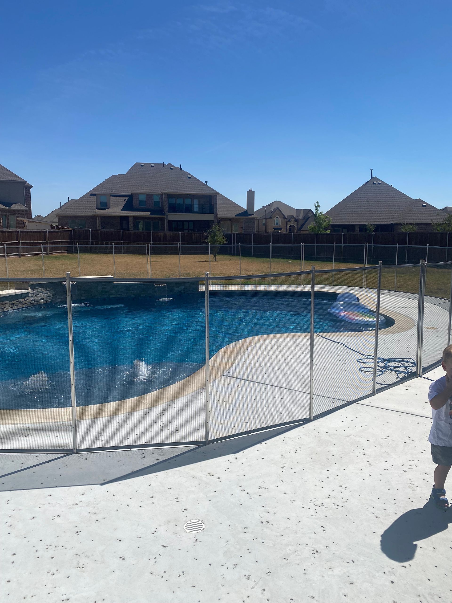 Resort pool with a safety fence, thatched-roof buildings, and a person at the right edge