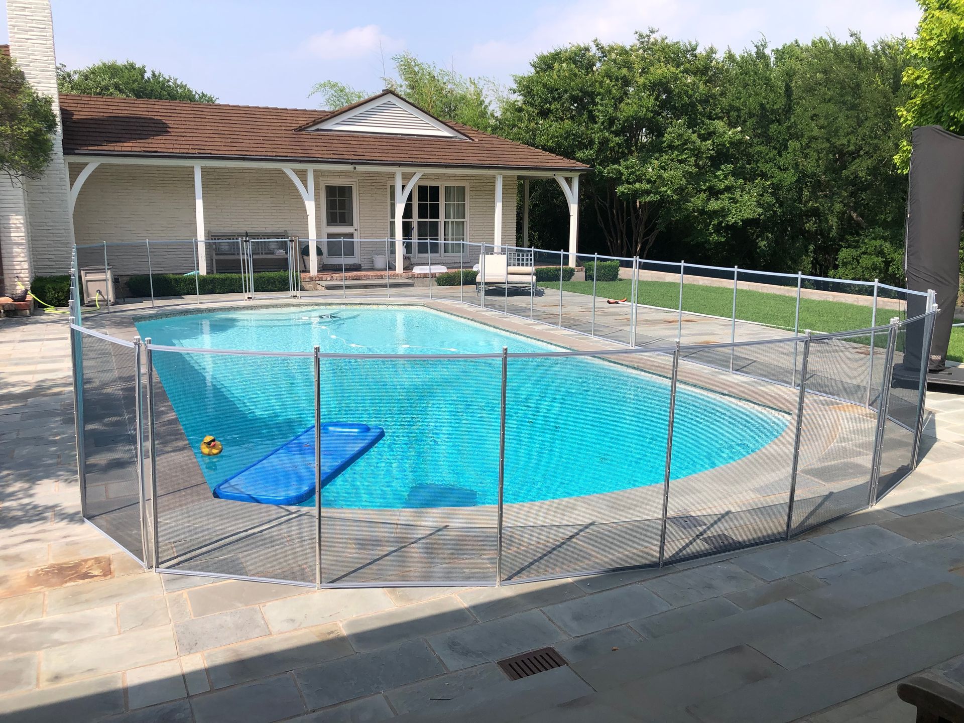 Backyard swimming pool with safety fence, patio, and house in the background