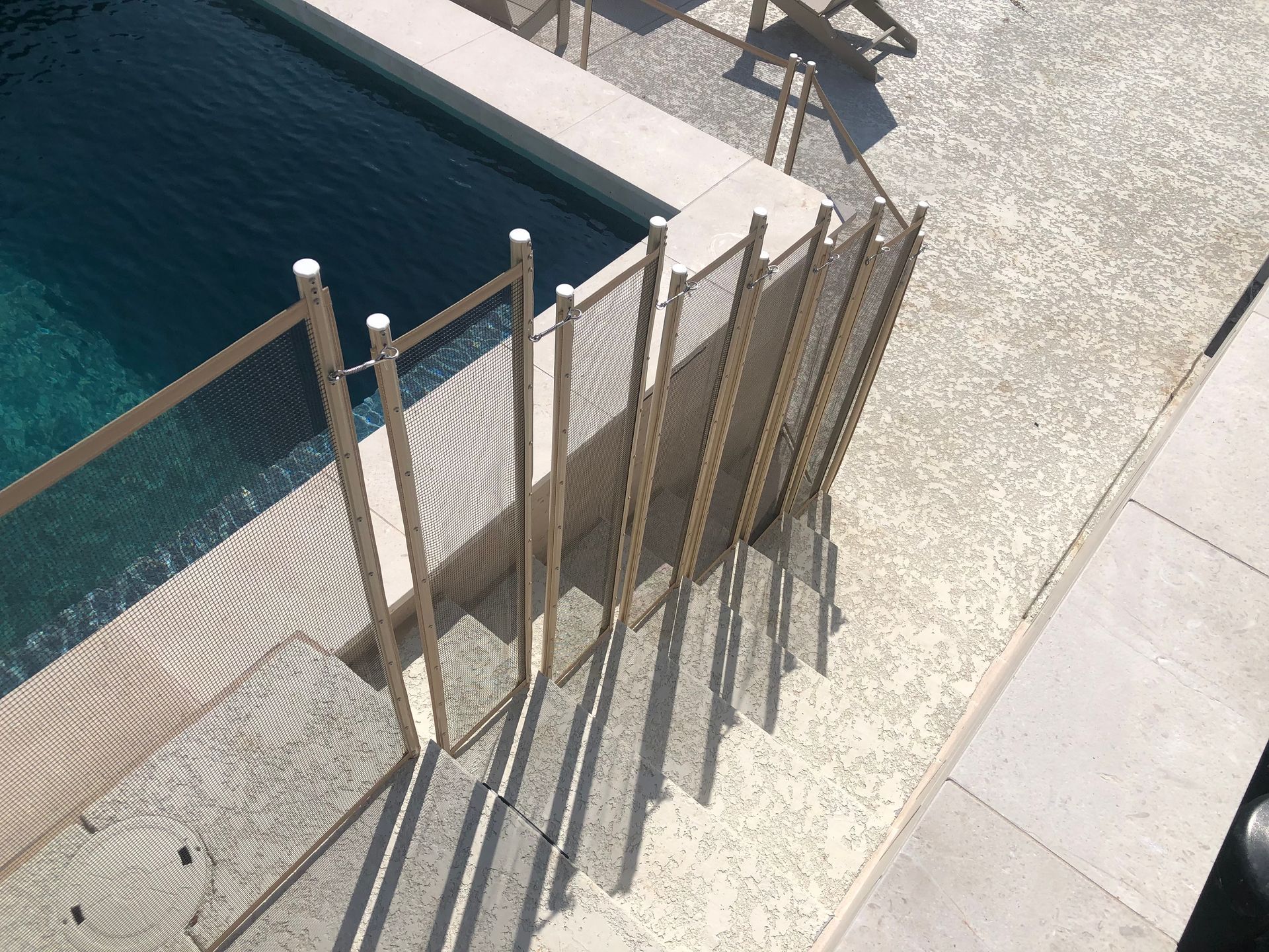 Wooden safety barrier beside a pool, with long shadows on a sunlit stone deck.