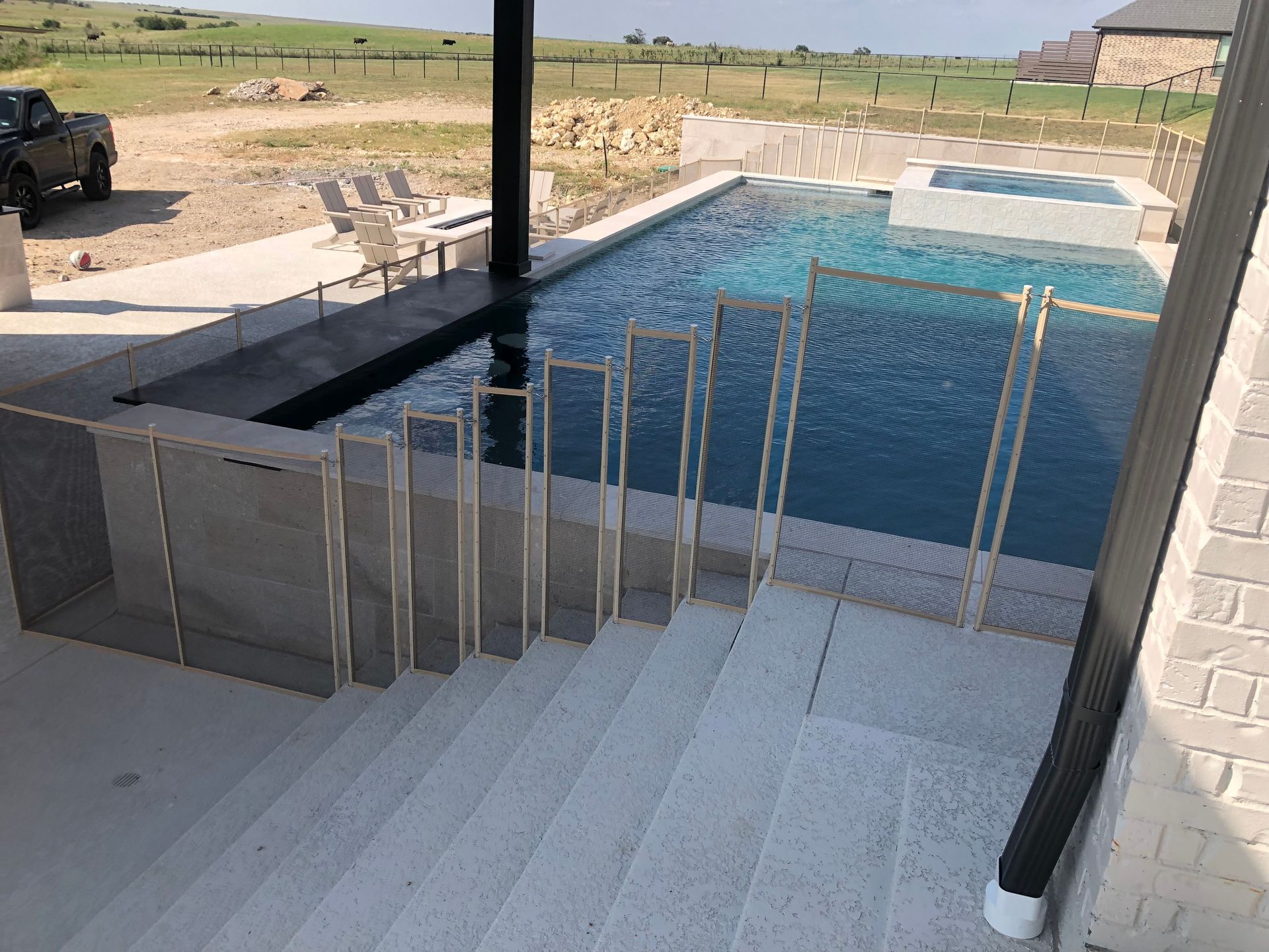 Steps descending to a backyard swimming pool with glass railing and countryside view