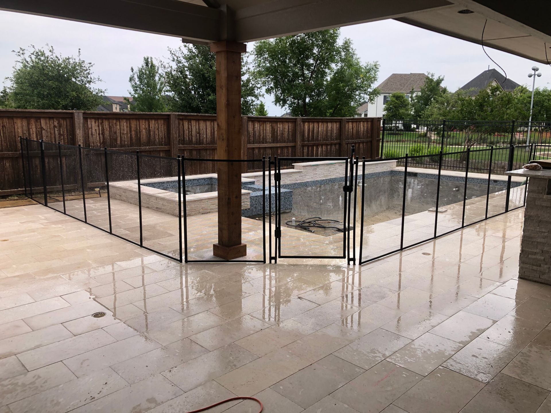 Covered patio with a fenced, empty pool or spa and wet stone floor after rain
