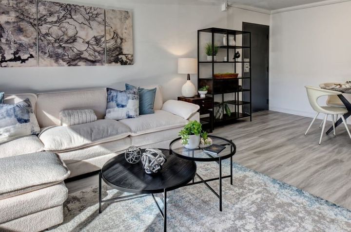 A living room with a couch , coffee table , chairs and a painting on the wall.