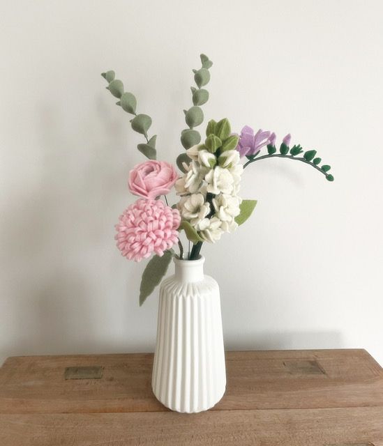 Witte vaas met vilten bloemen: roze hortensia, witte stokroos en groene eucalyptus op een houten tafel.
