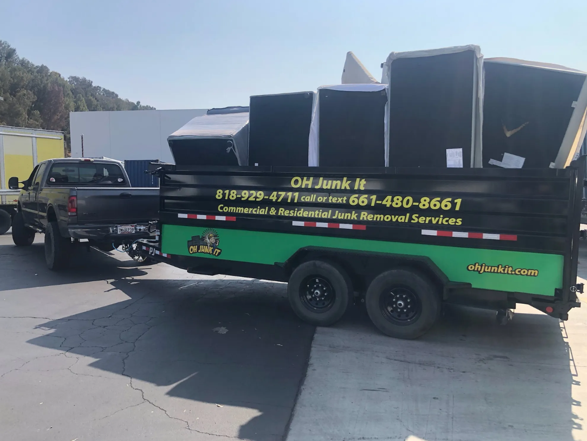 A truck towing a trailer loaded with junk, a sign reads 