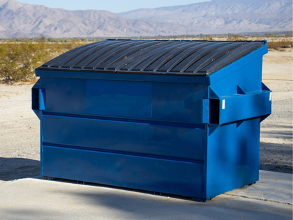 Blue dumpster with black roof, in a desert setting with mountains in the background.
