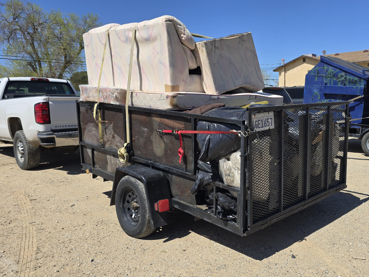 Pickup truck pulling a trailer loaded with furniture, secured with straps, outdoors.