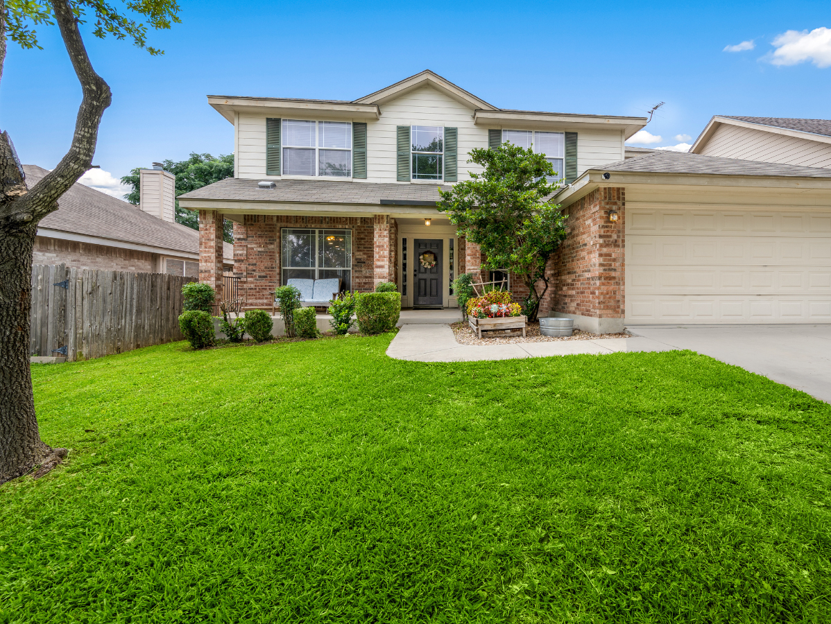 Two-story house with green lawn, brick accents, and a garage door, under a blue sky.