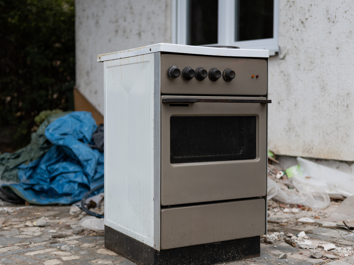 Gray and white electric stove in front of a weathered white building.