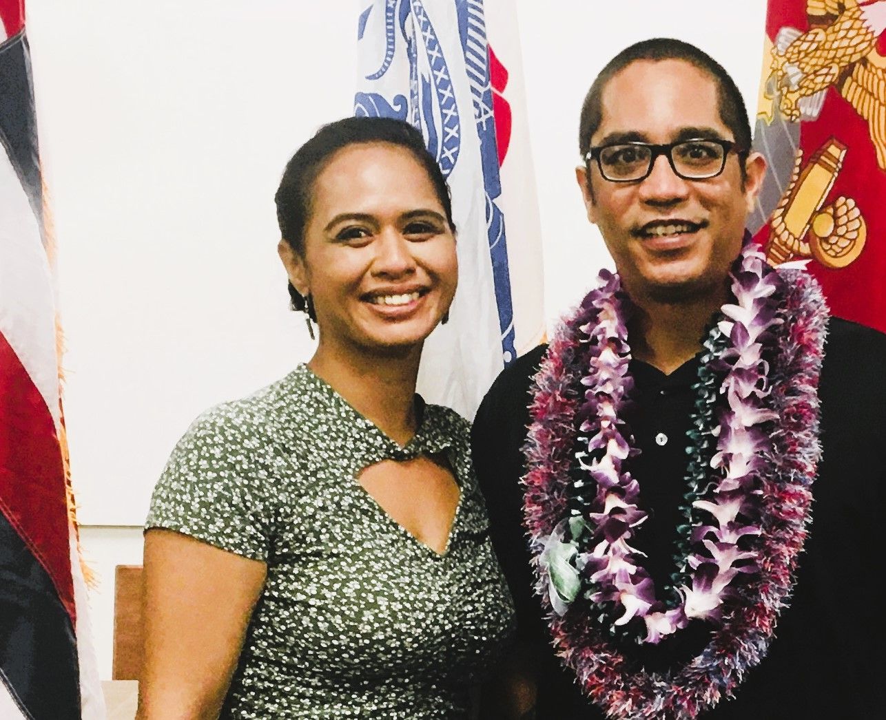A man and a woman are posing for a picture in front of a flag.