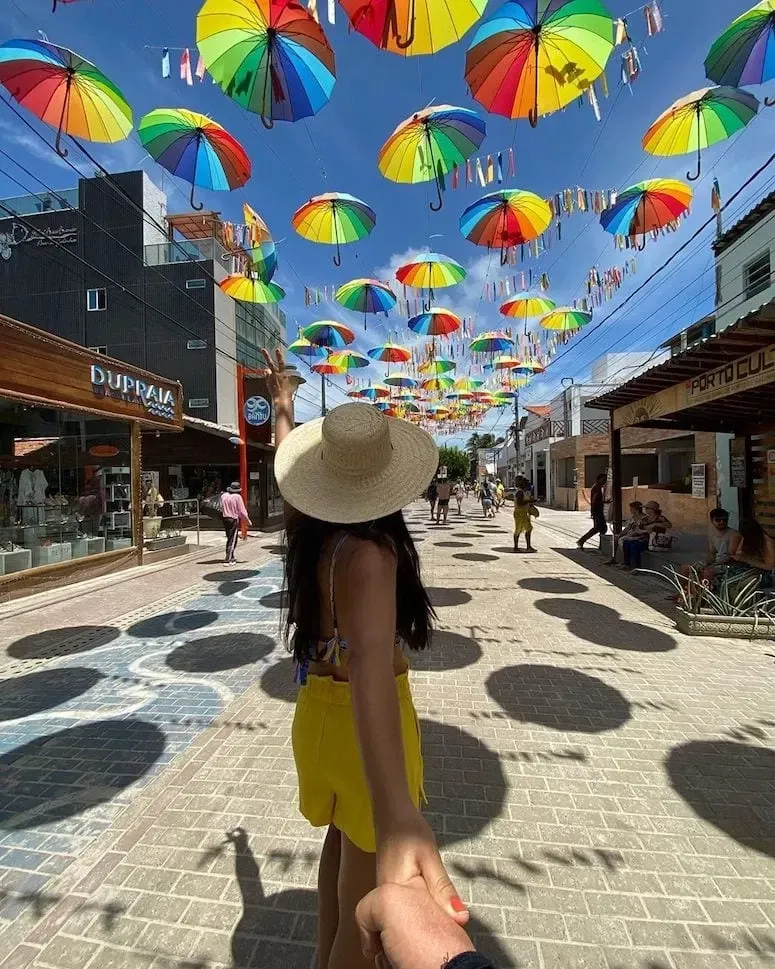 Uma mulher segura a mão de um homem enquanto caminha pela rua com guarda-chuvas pendurados no teto.
