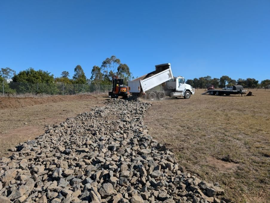 A Truck Unloading Lots of Rocks Into an Open Field — Ape Earthmoving In Westbrook, QLD