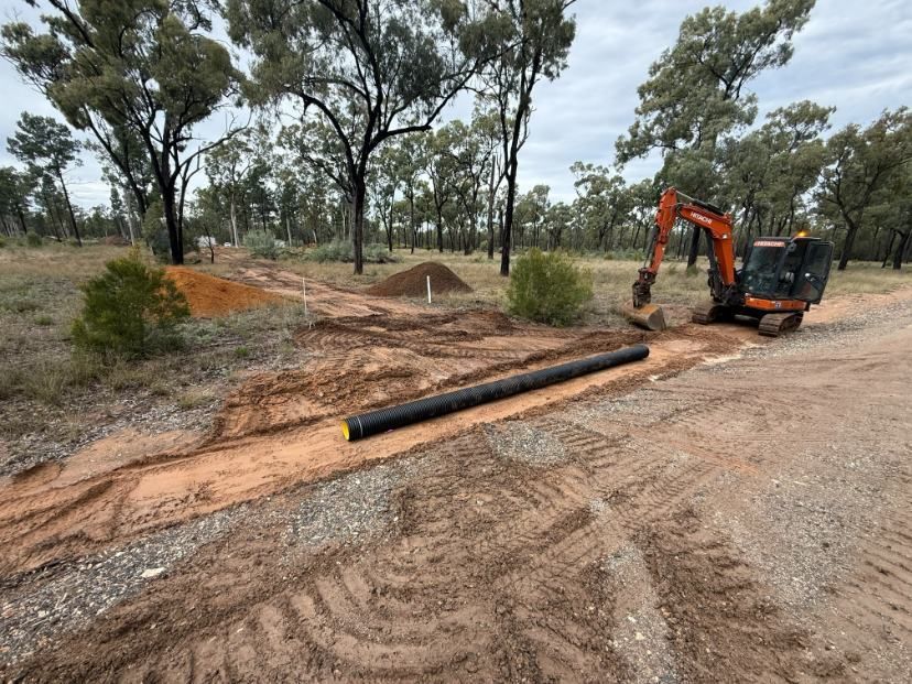 An Excavator is Digging a Hole in the Dirt Next to a Road — Ape Earthmoving In Westbrook, QLD