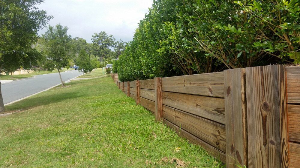 A Wooden Fence Surrounds a Lush Green Field Next to a Road — Ape Earthmoving In Highfields, QLD
