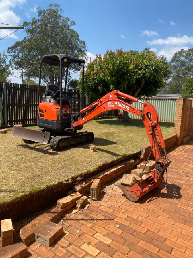 A Small Orange Excavator is Sitting on Top of a Brick Driveway — Ape Earthmoving In Westbrook, QLD