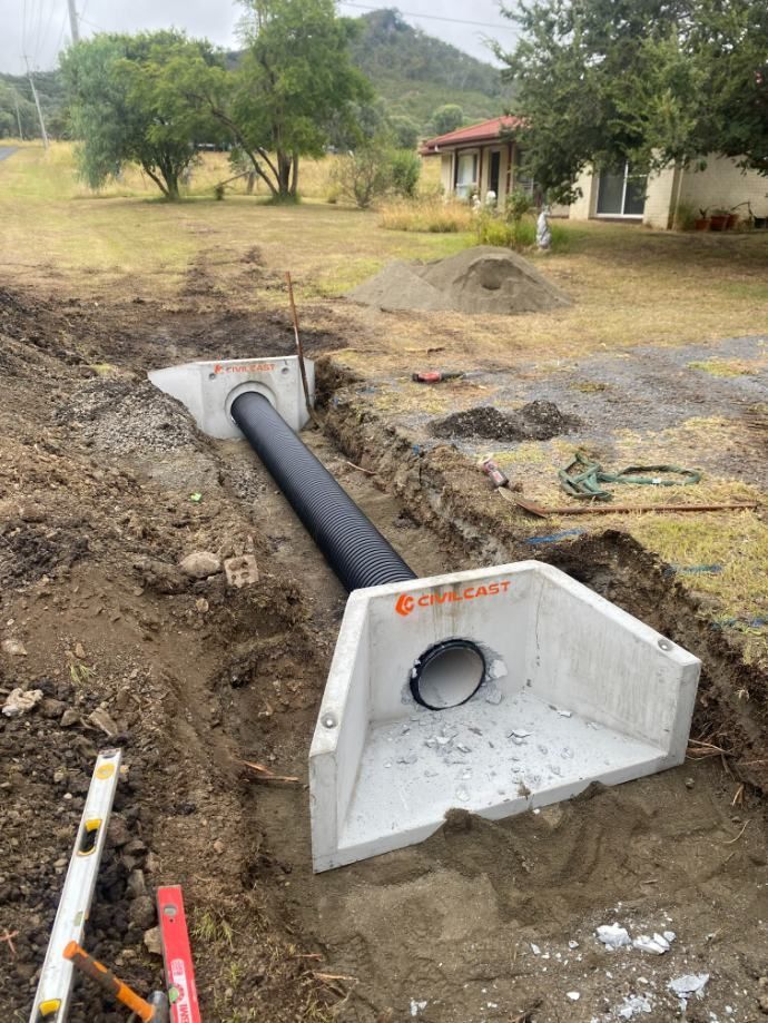 A Large Pipe is Being Installed in the Dirt in Front of a House — Ape Earthmoving In Westbrook, QLD
