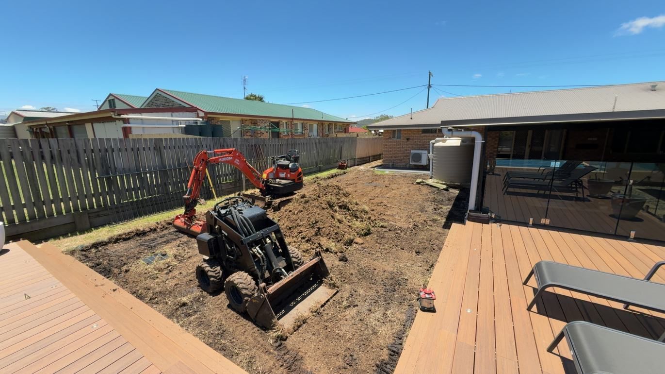 A Tractor is Digging a Hole in a Backyard Next to a House — Ape Earthmoving In Westbrook, QLD
