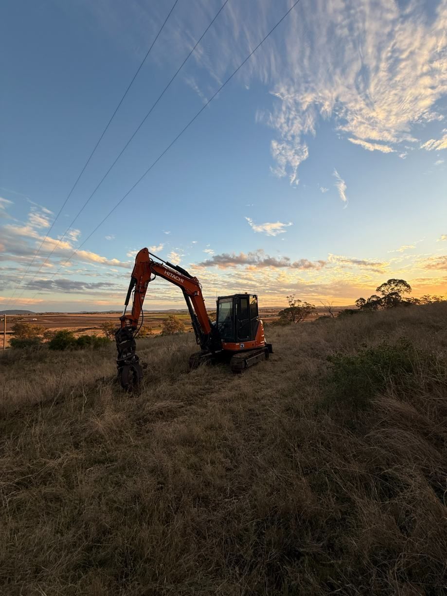 An Excavator is Sitting in the Middle of a Field at Sunset — Ape Earthmoving In Westbrook, QLD